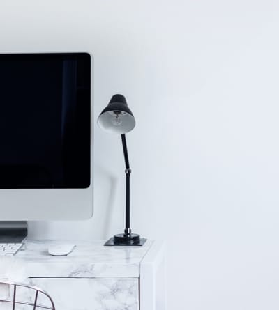 online_store_30 | Stanter White marble desk with an iMac, keyboard and mouse, and a black adjustable desk lamp against a pale wall—a clean workstation.